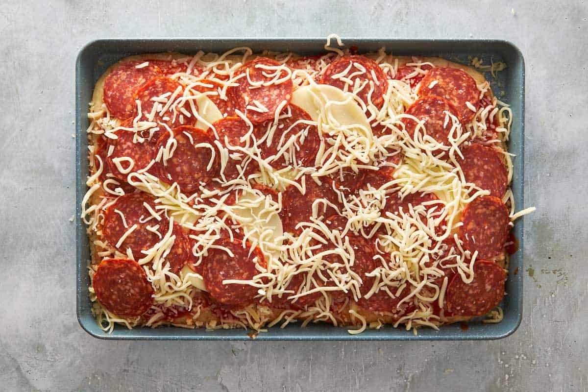 Unbaked pepperoni focaccia pizza topped with tomato sauce, mozzarella, and provolone before baking.