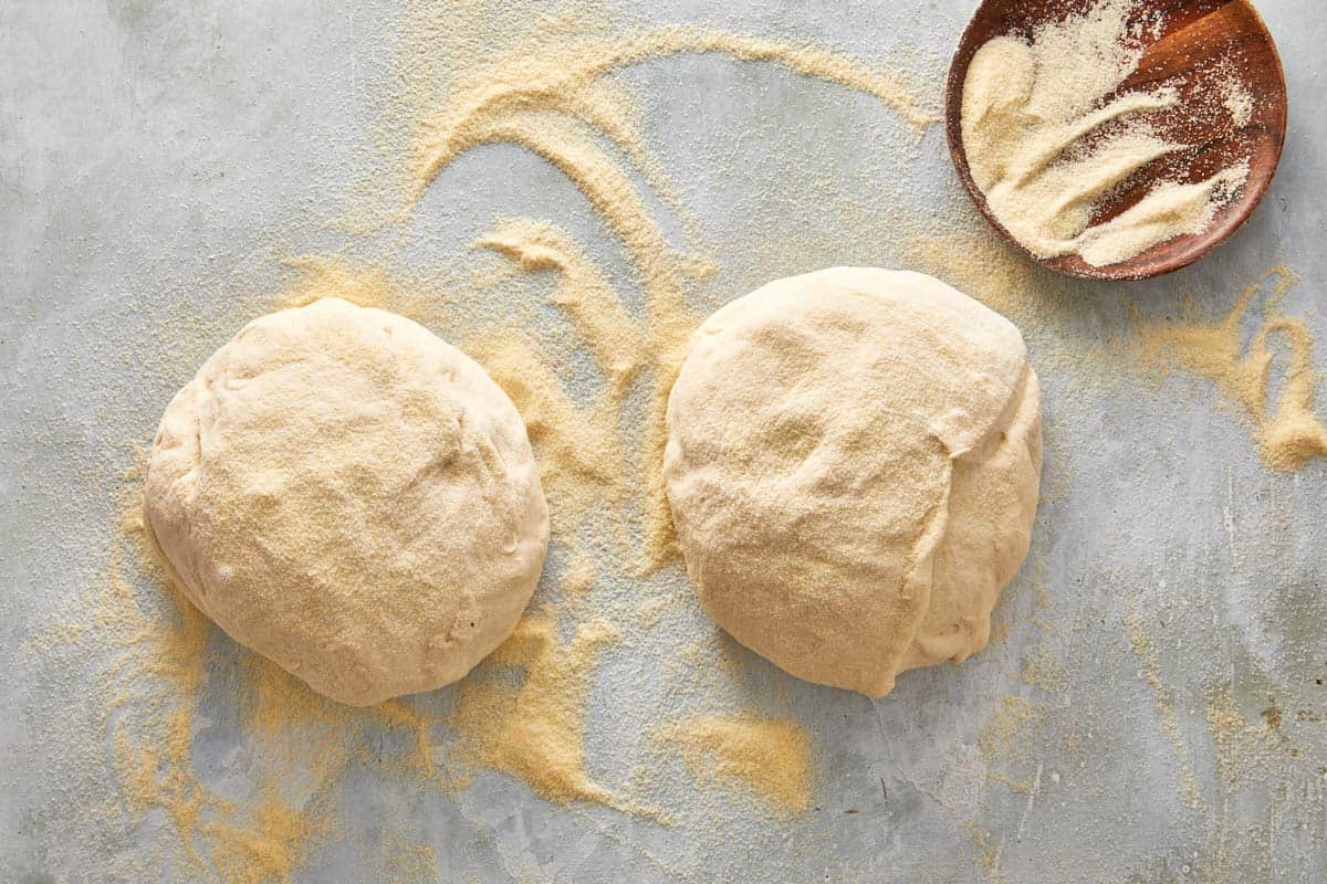 Two portions of focaccia dough dusted with semolina flour on a floured surface, ready to shape.