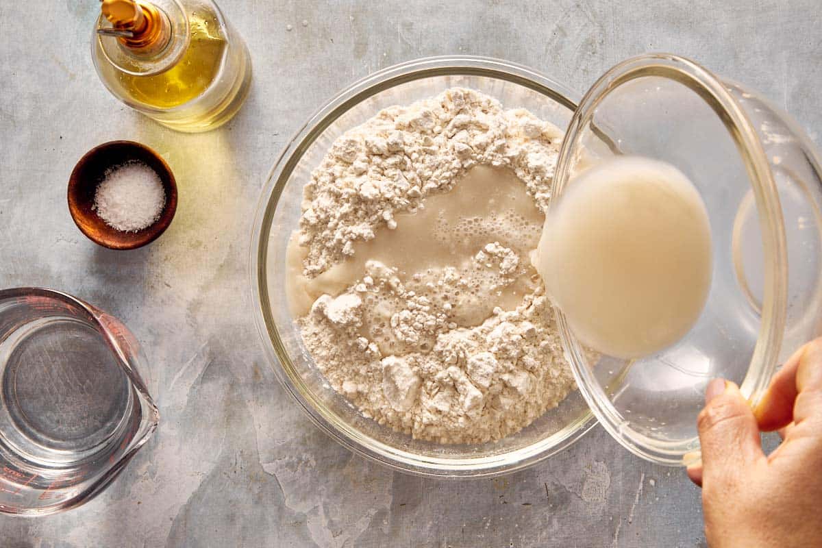 Pouring yeast mixture into a bowl of flour to start making focaccia dough.