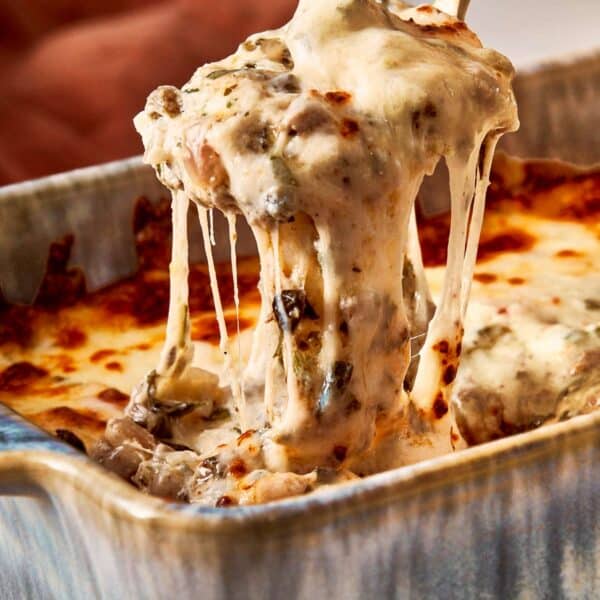 Spoon lifting hot, melted lasagna dip with gooey cheese.