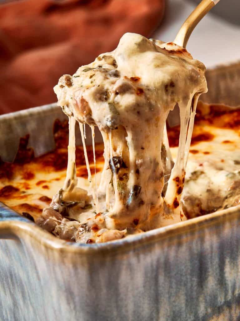 Spoon lifting hot, melted lasagna dip with gooey cheese.