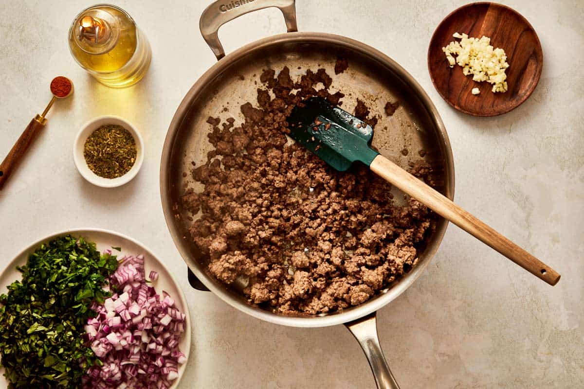 Ground beef cooking in a pan with onions and herbs.