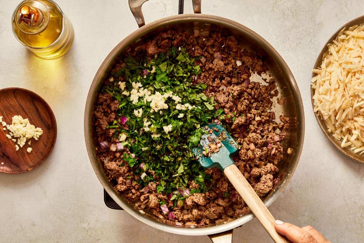Stirring fresh herbs and garlic into the meat mixture.