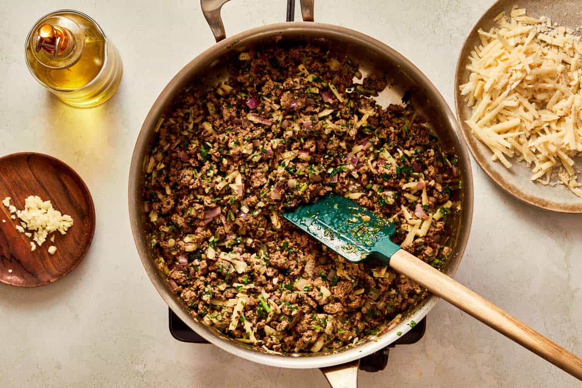 Cooked beef mixed with herbs and Parmesan in a pan.