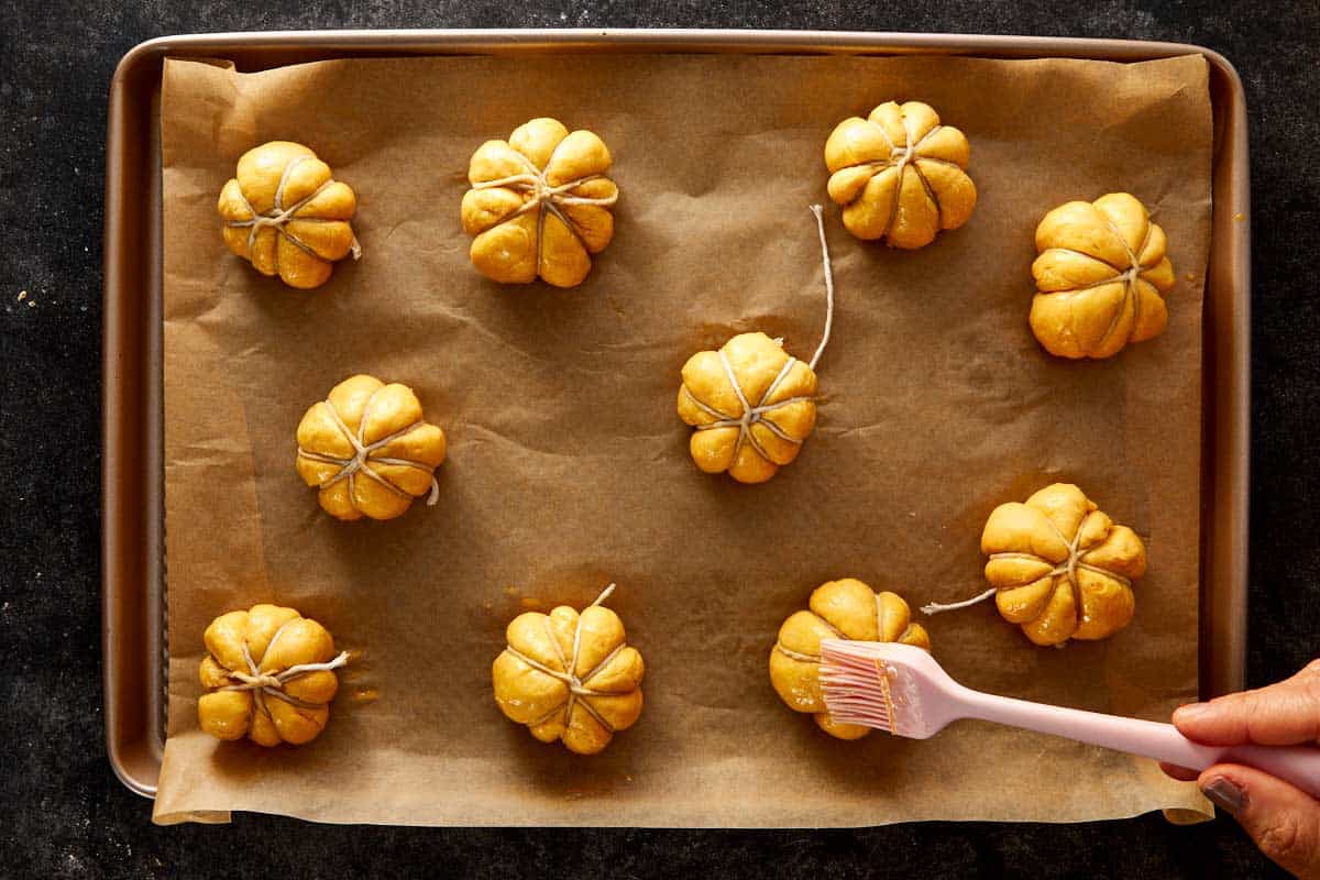 Pumpkin-shaped dough balls tied with kitchen twine and brushed with egg wash on a baking tray.