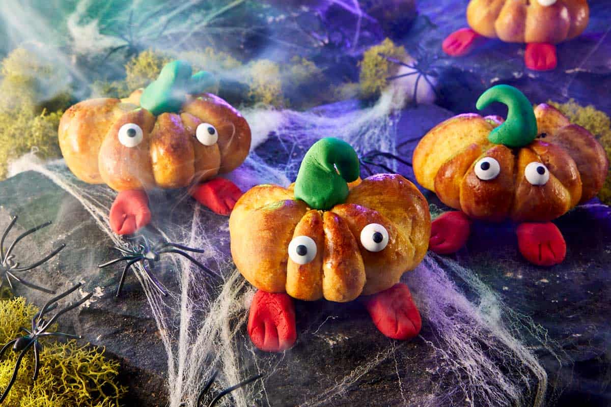 Decorated pumpkin breads with fondant stems and candy eyes arranged on a spooky Halloween setup.