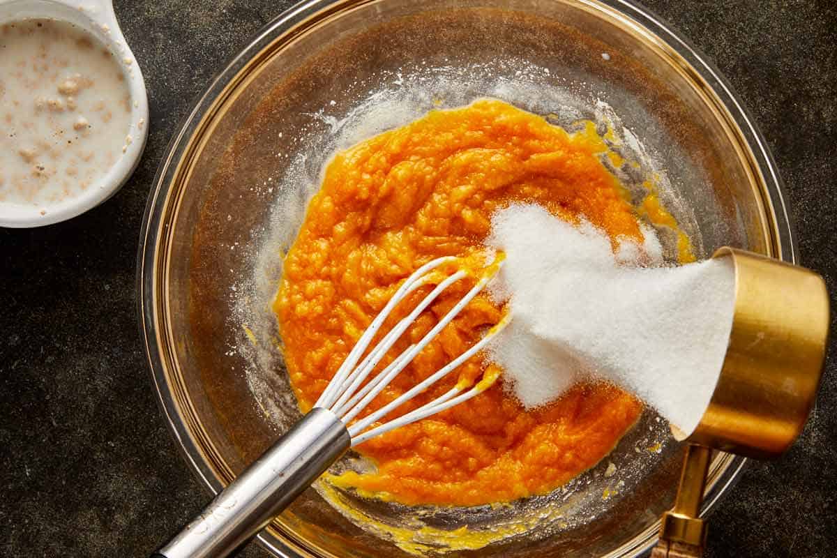 Pumpkin purée and sugar being mixed in a glass bowl with a whisk for the pumpkin bread dough.