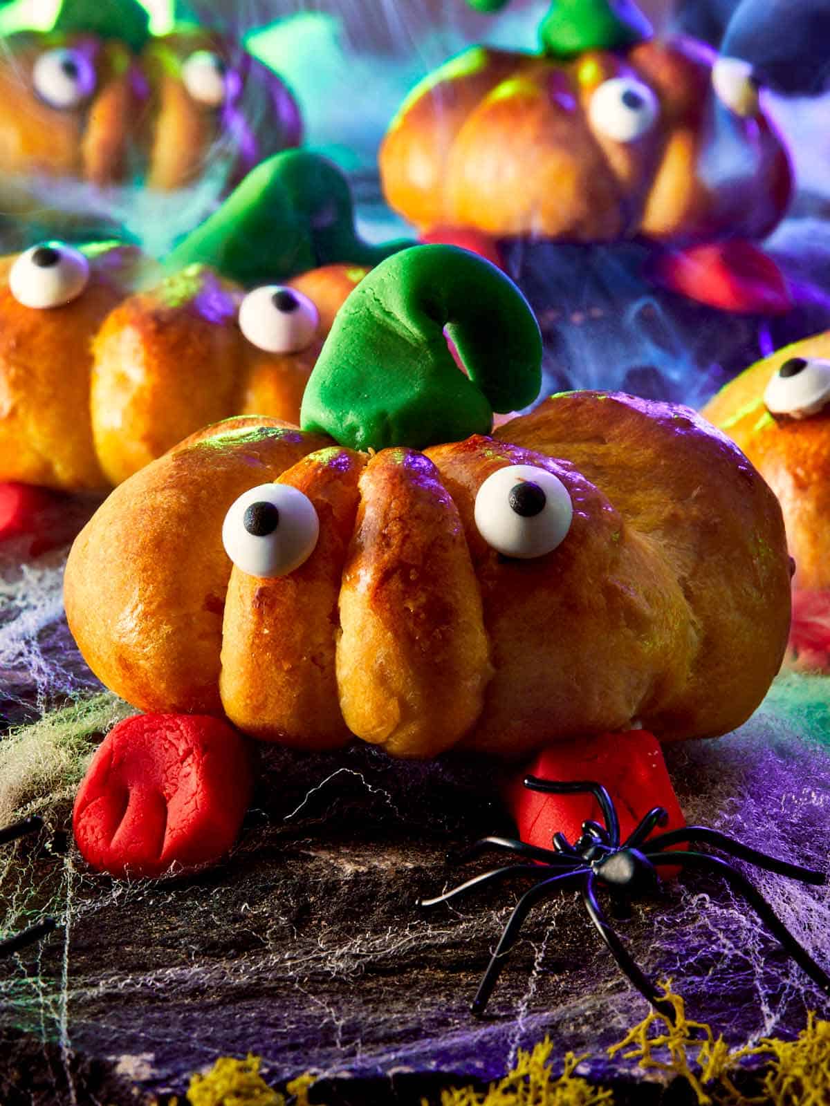 Close-up of finished pumpkin breads with green fondant stems and red fondant feet, surrounded by Halloween props.