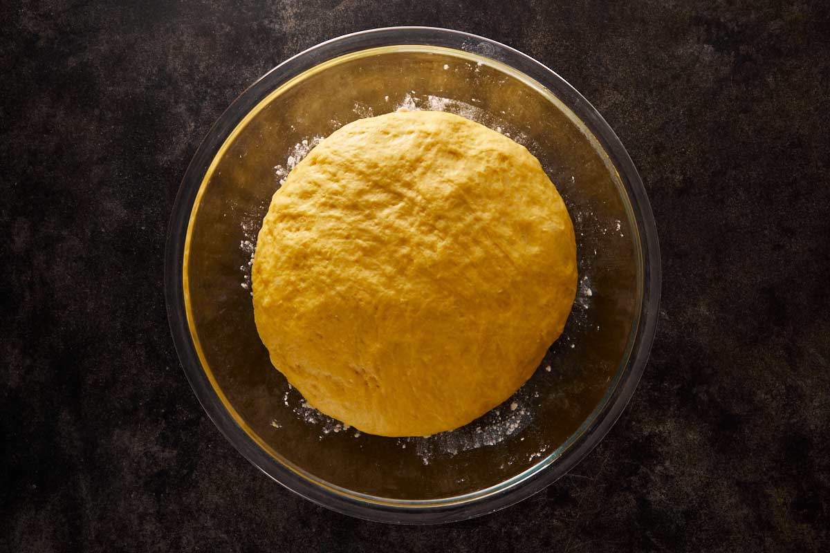 Risen pumpkin bread dough in a glass bowl, fluffy and ready to shape.