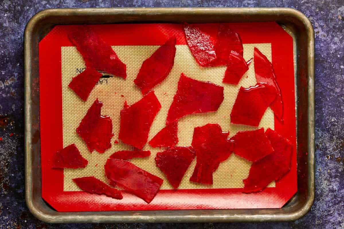 Tray of bright red caramel shards resembling broken glass cooling on a silicone mat, ready for decoration.