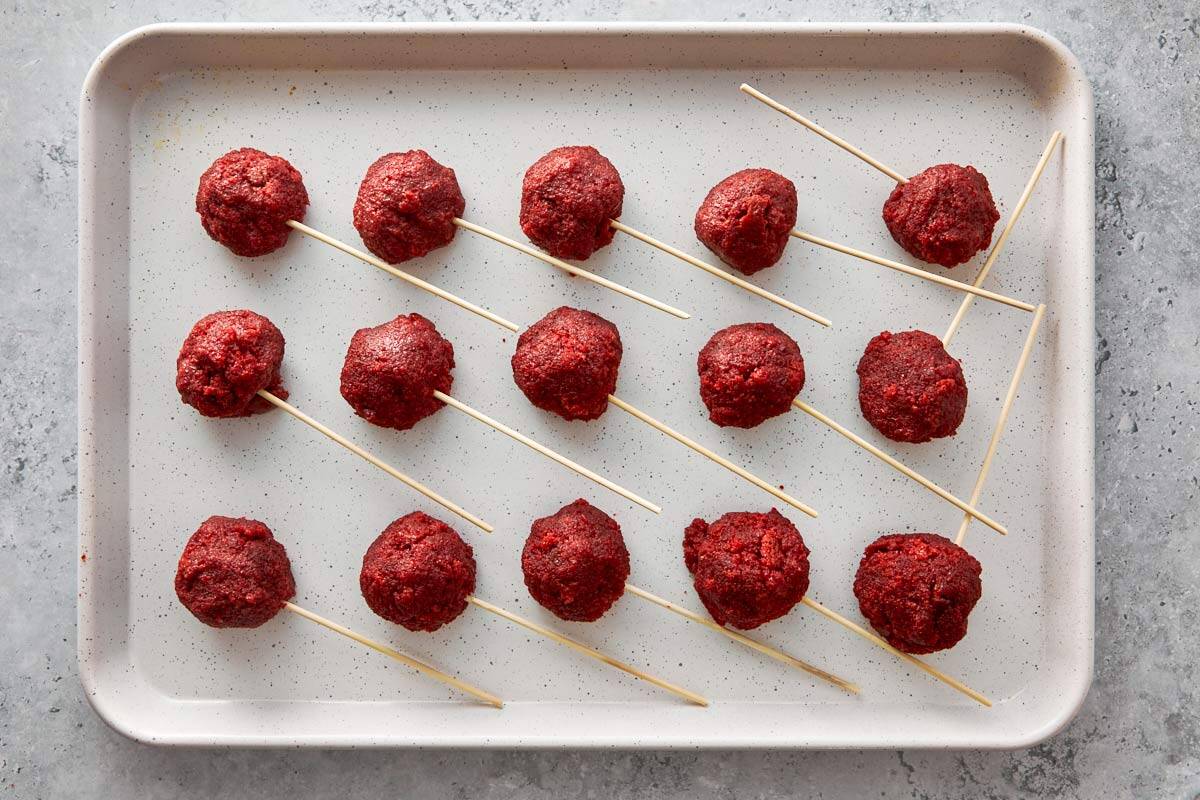 Red velvet cake pops shaped into balls with sticks on a baking tray.