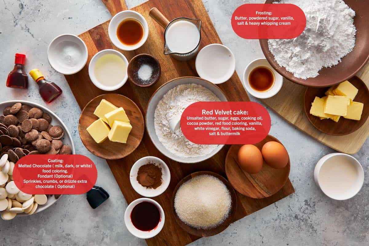 Ingredients for Red Velvet Monster Cake Pops including butter, sugar, eggs, cocoa powder, red food coloring, flour, buttermilk, chocolate, and frosting ingredients labeled on a wooden board.