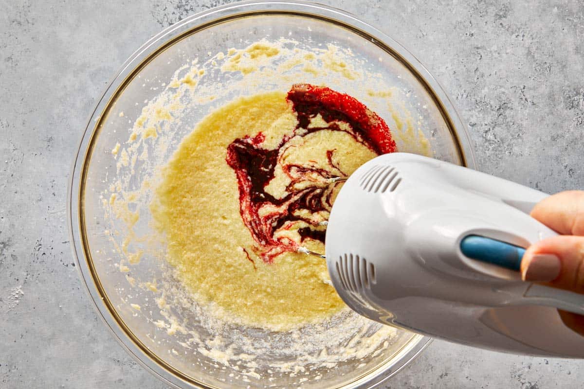 Mixing red velvet batter with cocoa and red food coloring in a glass bowl.