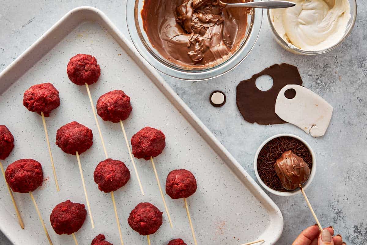 Dipping red velvet cake pops into melted chocolate and sprinkles.