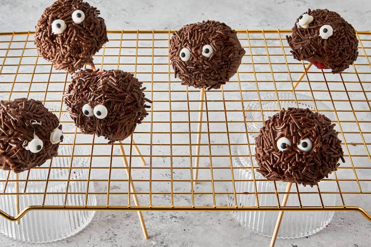 Decorated monster cake pops with candy eyes setting on a cooling rack.