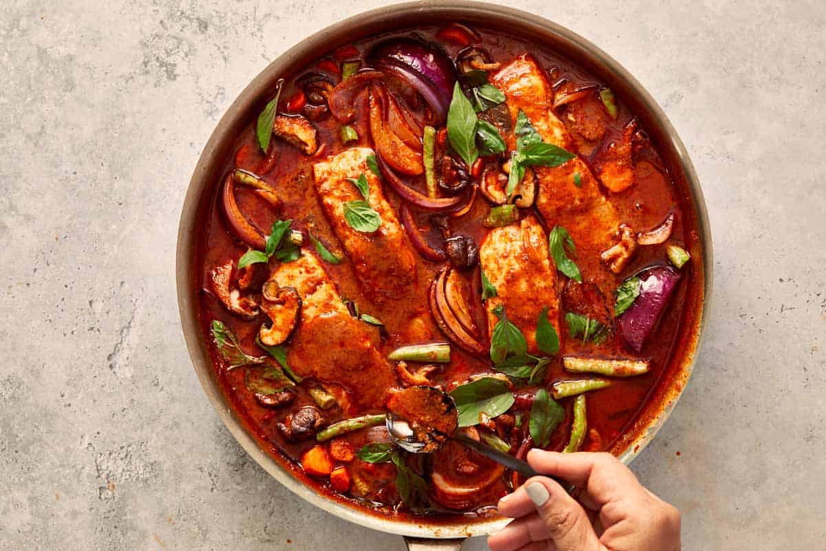 Salmon fillets simmering in the rich curry with vegetables, while fresh basil and kaffir lime leaves are stirred in for aroma.