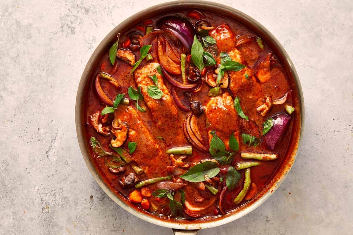 Final simmer of Salmon Panang Curry — a vibrant red sauce filled with salmon, basil, and colorful vegetables ready to serve.