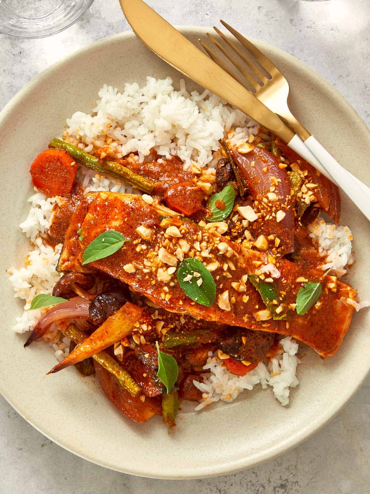 Overhead shot of Salmon Panang Curry served over jasmine rice. Tender salmon fillets coated in a rich red curry sauce with peanuts, basil leaves, and vegetables.