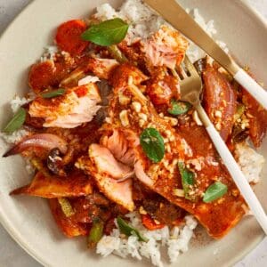 Overhead shot of Salmon Panang Curry served on a plate with jasmine rice. The salmon is coated in a rich red curry sauce, topped with crushed peanuts and fresh Thai basil leaves, with gold cutlery resting on the side.