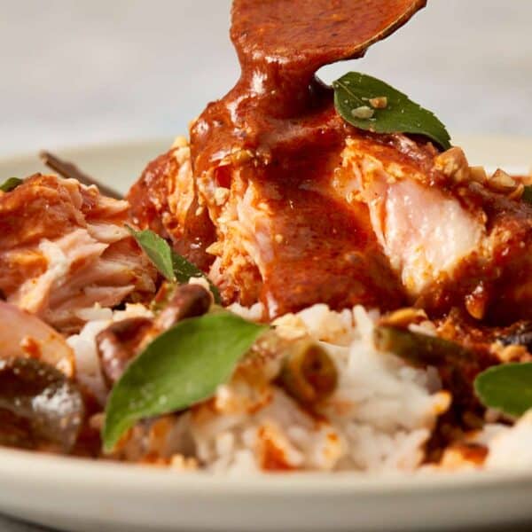 Close-up of golden curry sauce being spooned over salmon and rice, highlighting the creamy texture, kaffir lime leaves, and glossy finish of the Panang curry.