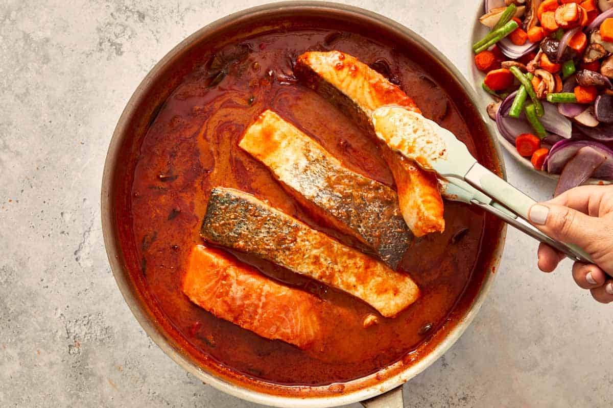 Salmon fillets cooking skin-side down in the simmering Panang curry sauce, slowly turning golden and tender.