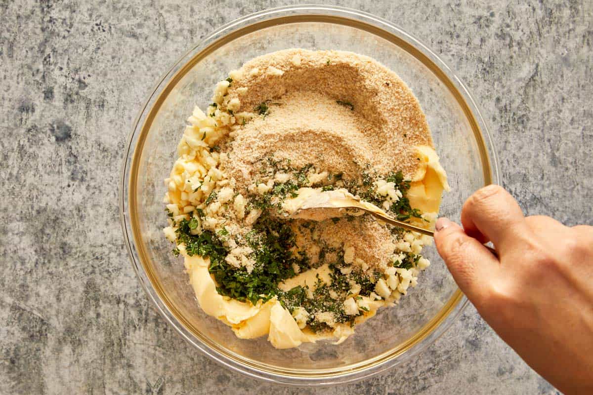Mixing softened butter, chopped garlic, parsley, salt, and breadcrumbs in a bowl to make garlic parsley butter.