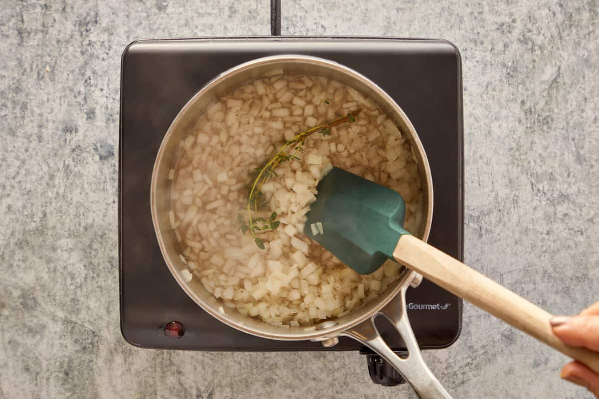 Simmering chopped onions with thyme and white wine in a saucepan to create a fragrant base.