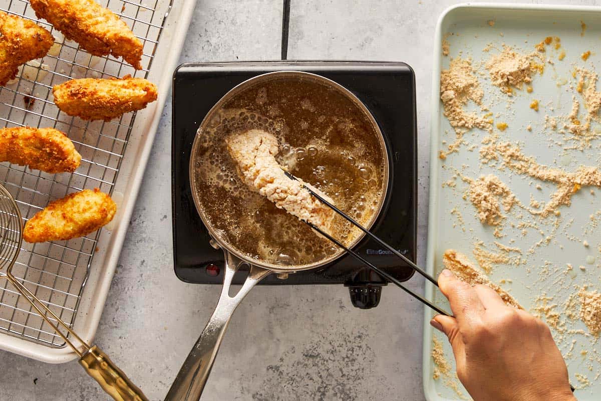 Hand frying breaded fish fillet in hot oil with golden pieces draining on a rack