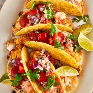 Crispy fish tacos topped with pico de gallo, cilantro, and lime wedges on a plate