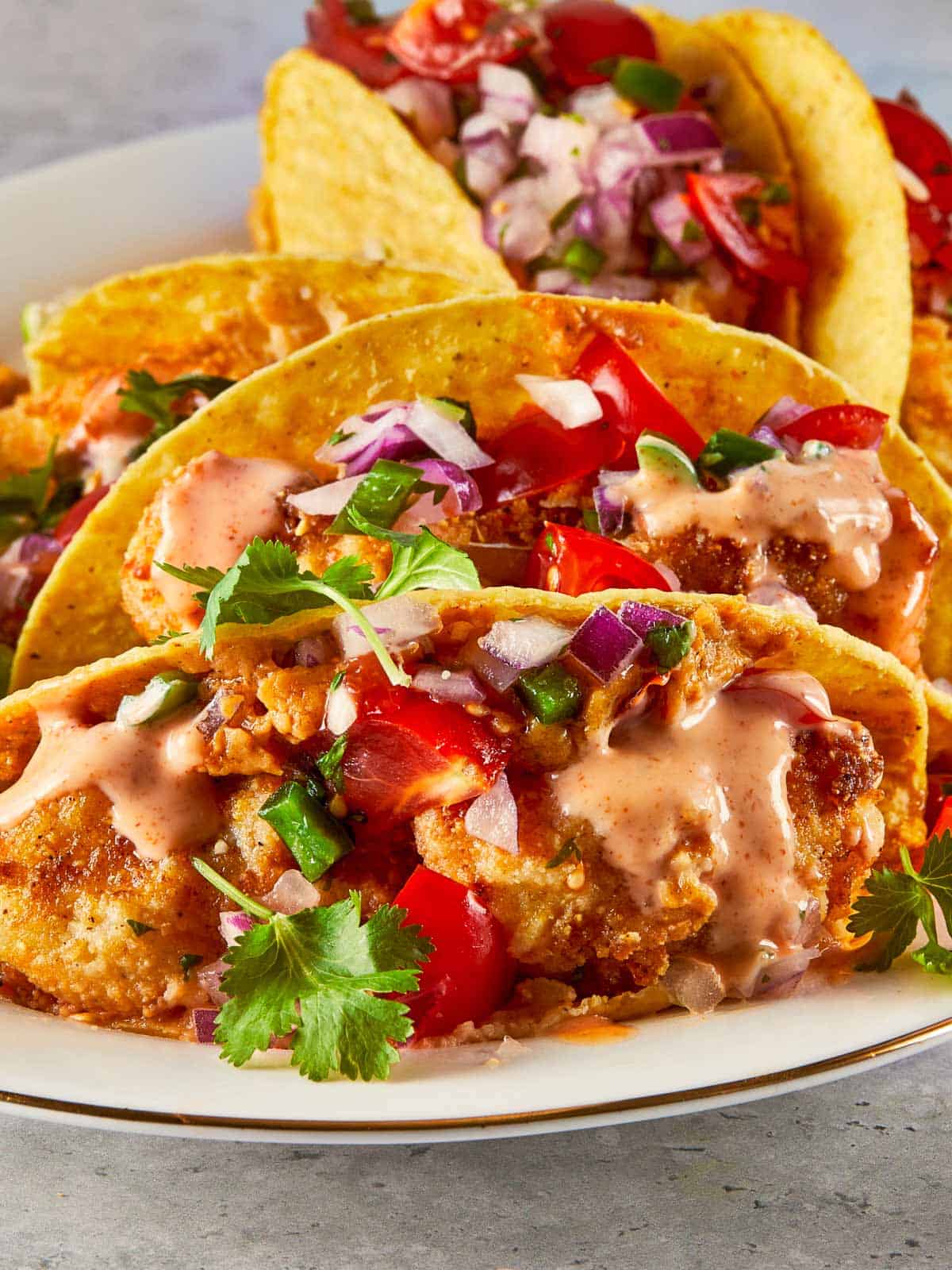 Close-up of crispy fish tacos topped with pico de gallo, cilantro, and spicy mayo
