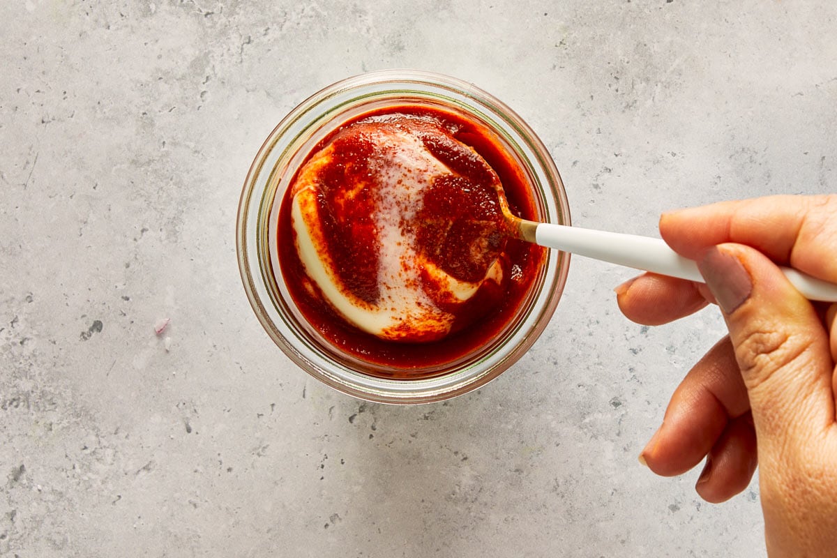 Hand mixing mayonnaise with sriracha in a small glass bowl