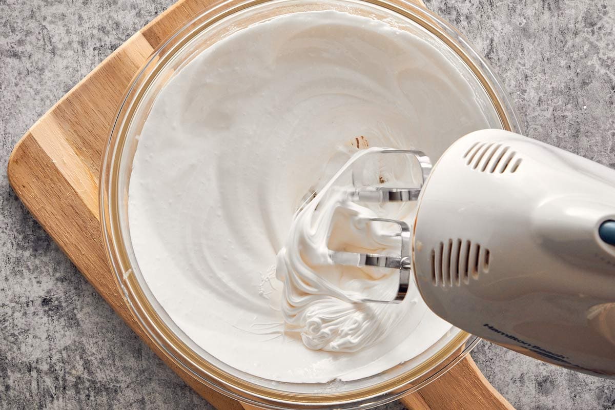 Whipping glossy Swiss meringue with an electric mixer until stiff peaks form.