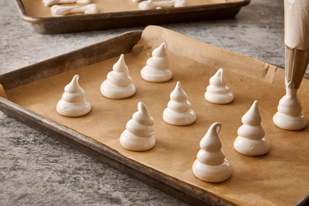 Piping ghost shapes of meringue onto parchment-lined baking trays.