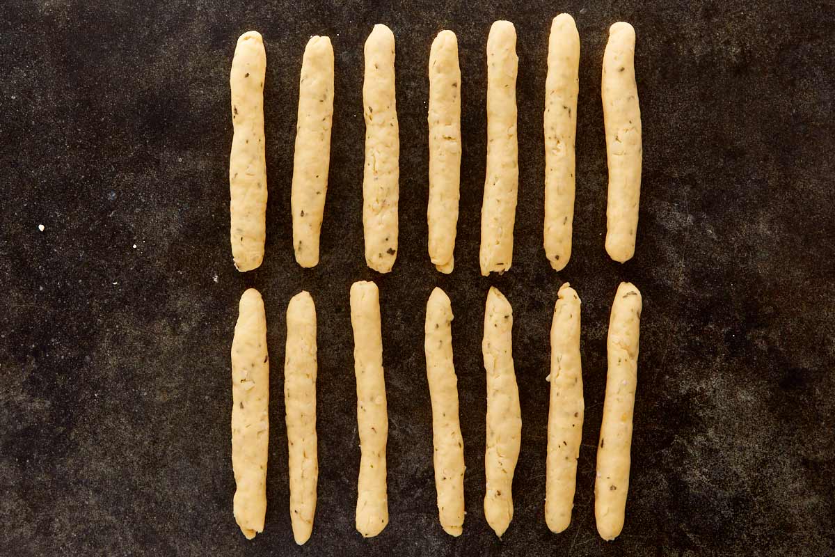 Rows of rolled dough shaped like fingers on a dark surface, ready to transform into witchy grissini.