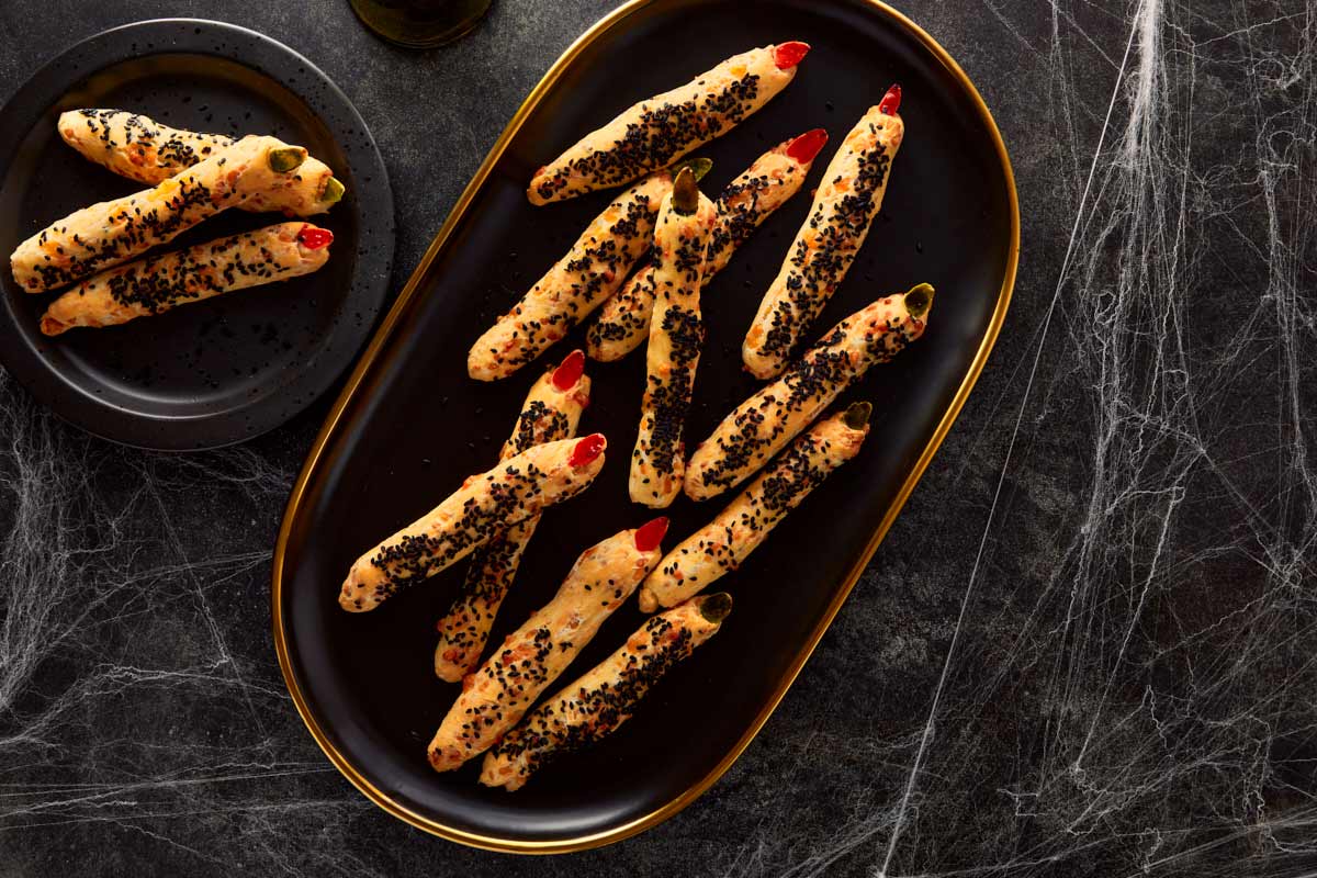 Golden baked witch finger grissini on a black platter, surrounded by cobwebs — crispy and eerie perfection.