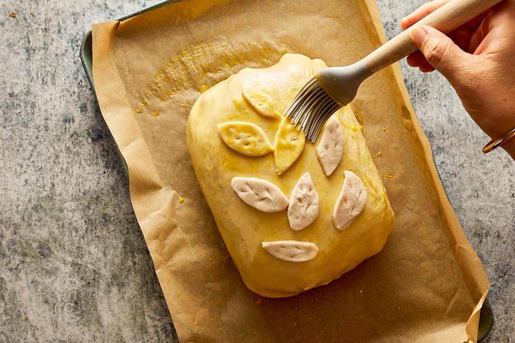 pastry covered with decorated pastry in the shape of small leaves being brushed with egg to form a layer that will be cooked and used to brown the pastry.