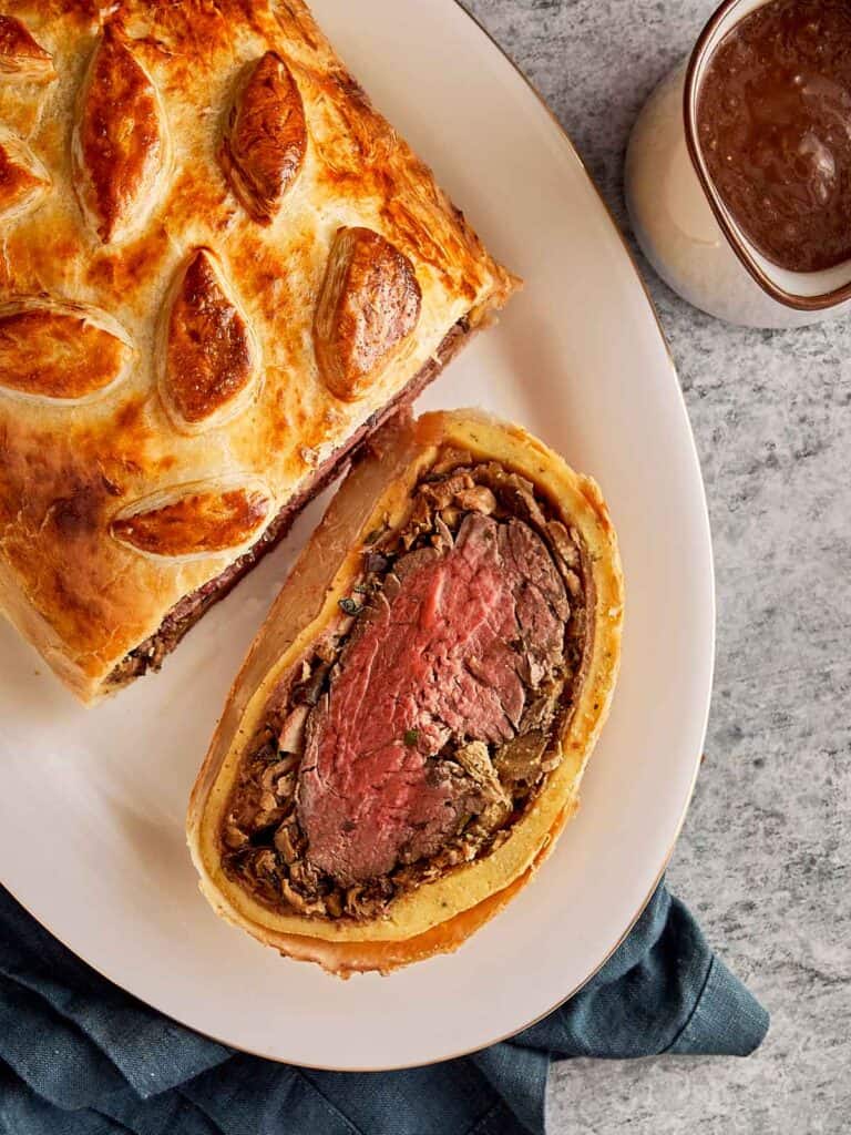 a cut piece of beef Wellington on a plate with the pink meat showing