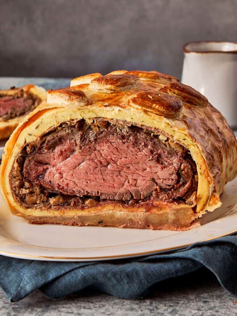 delicious beef wellington on a plate with cut in half exposing the pink meat inside covered with a delicious pastry