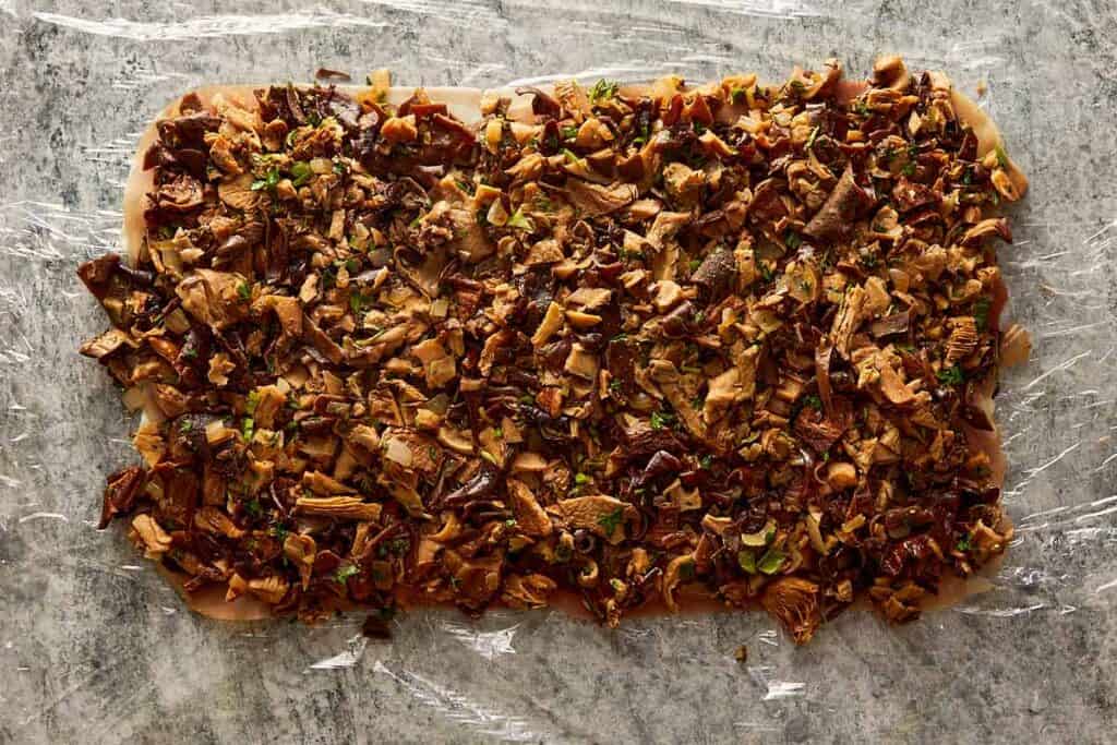 chopped mushrooms layed down on the plastic wrap in a rectangle