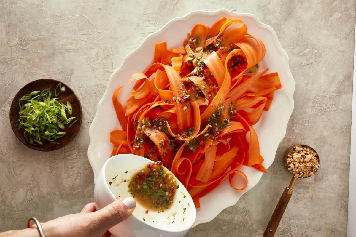 shredded carrots served in a bowl with seasoning bring poured ontop of it