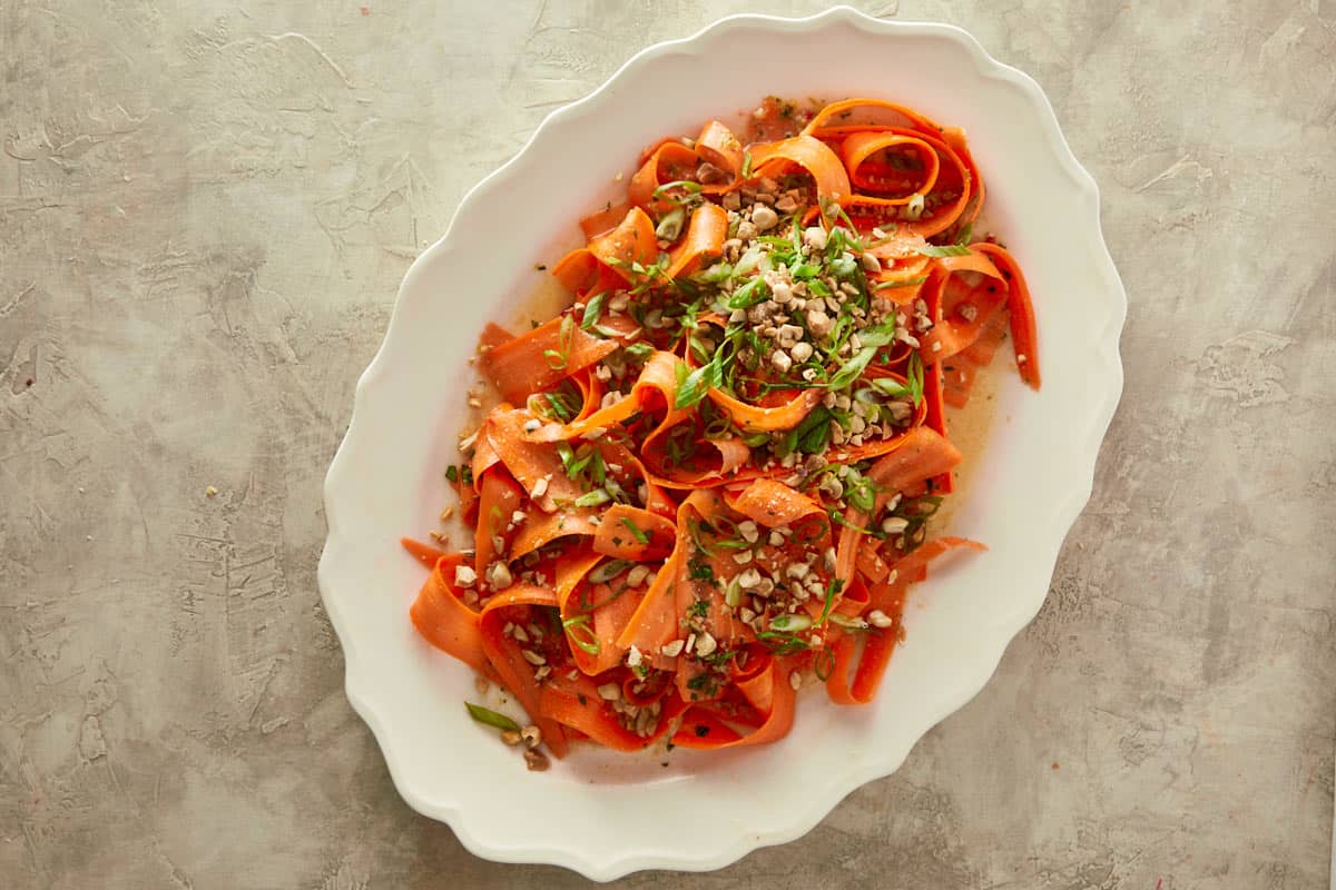 carrot salad finished served in a bowl with peanuts and green onion being sprinkled over it