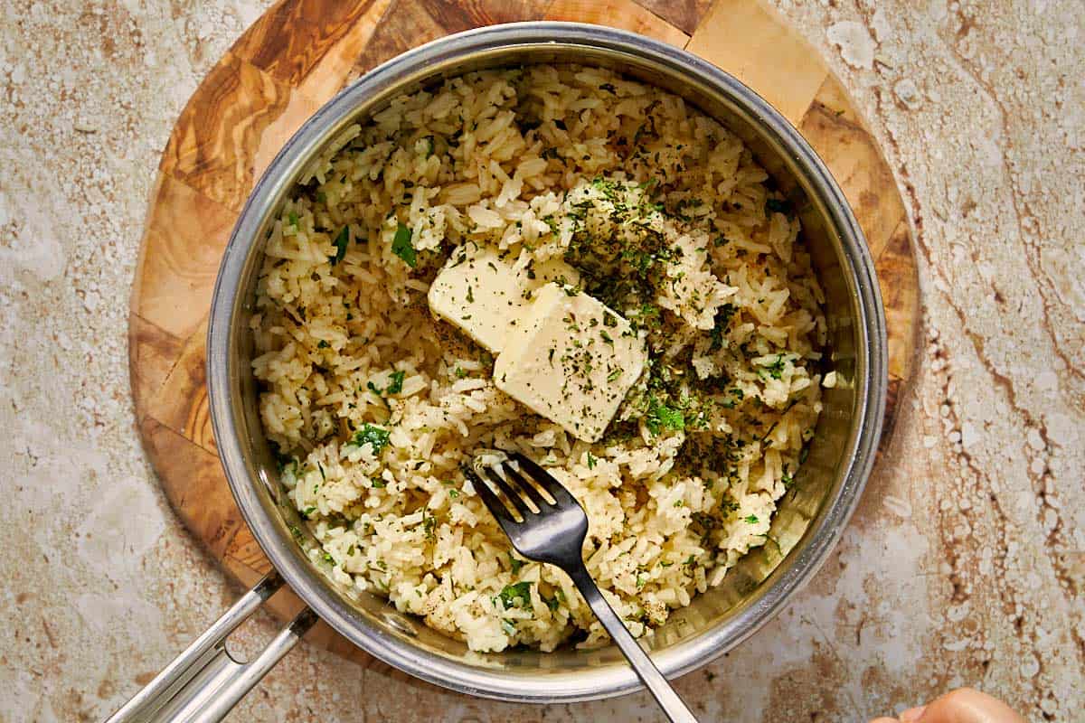 rice being cooked in a pot with garlic butter and parsley