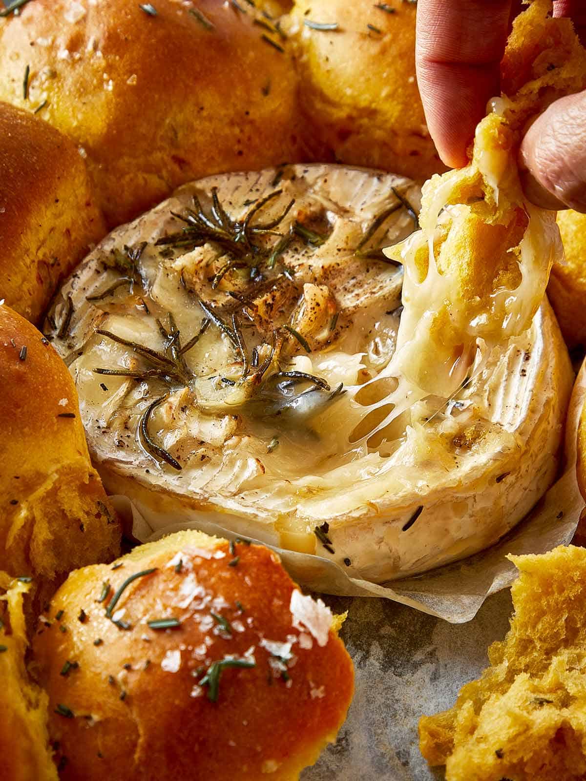 close up of a sweet potato bun being dipped into a wheel of melted cheesy dip