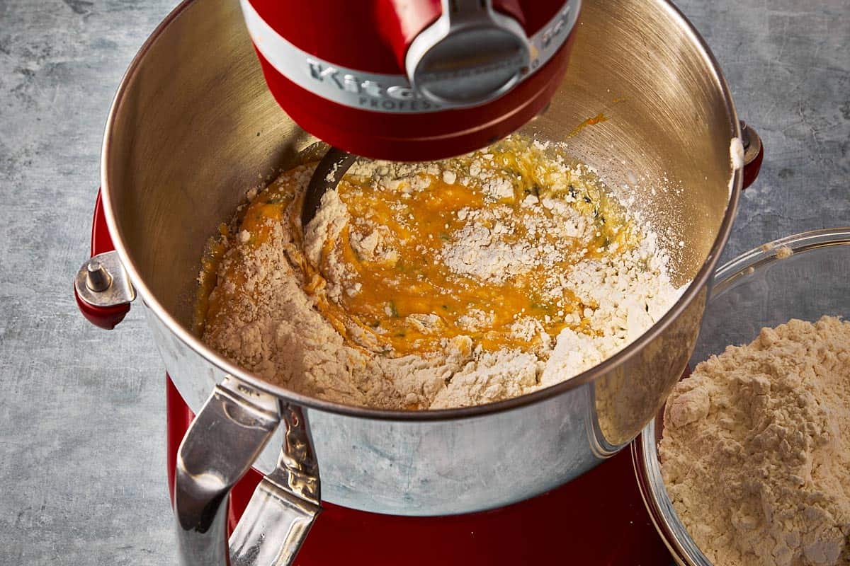 a stand mixer with the base of a bread dough with flour gradually being added in