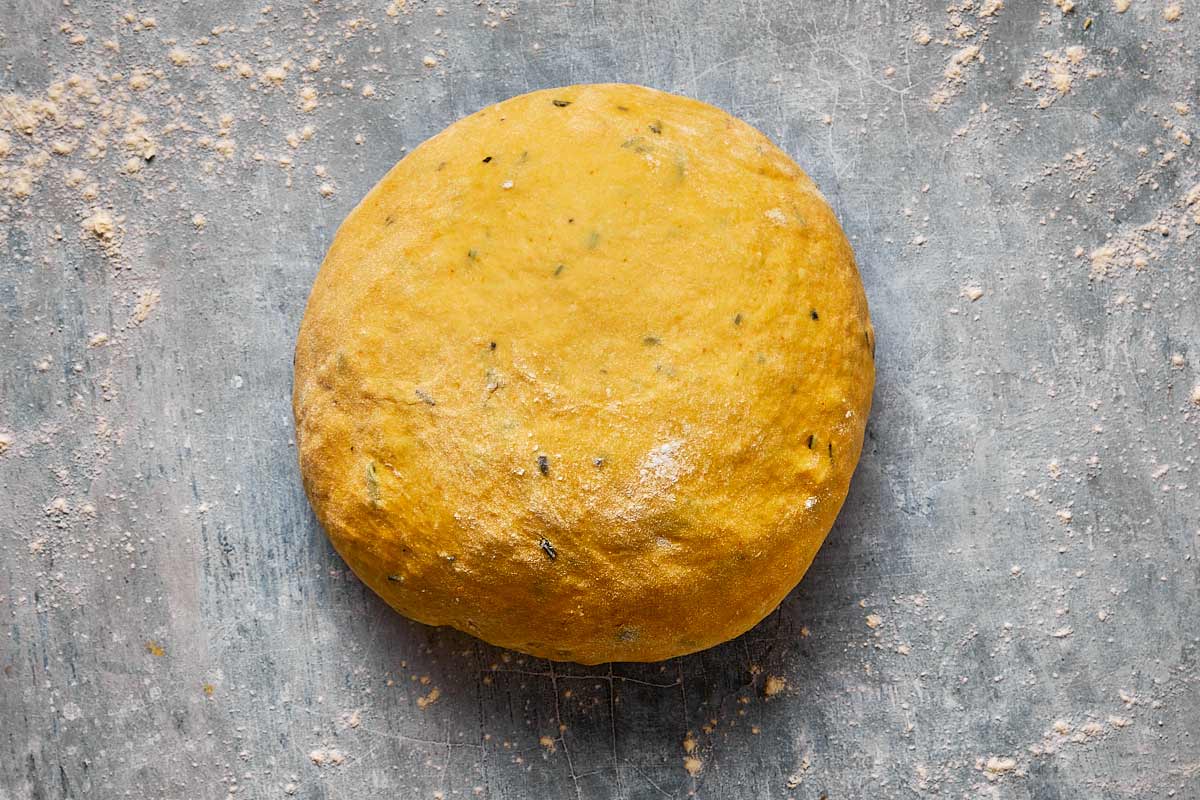 a ball of bread dough laid flat on a bench with flour on it