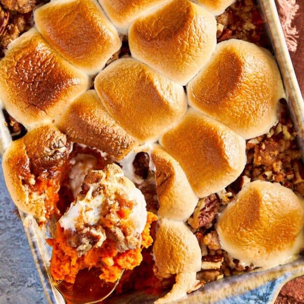 Sweet potato casserole with toasted marshmallows on top, with a spoon lifting a scoop showing the creamy sweet potato layer and crunchy pecan streusel.