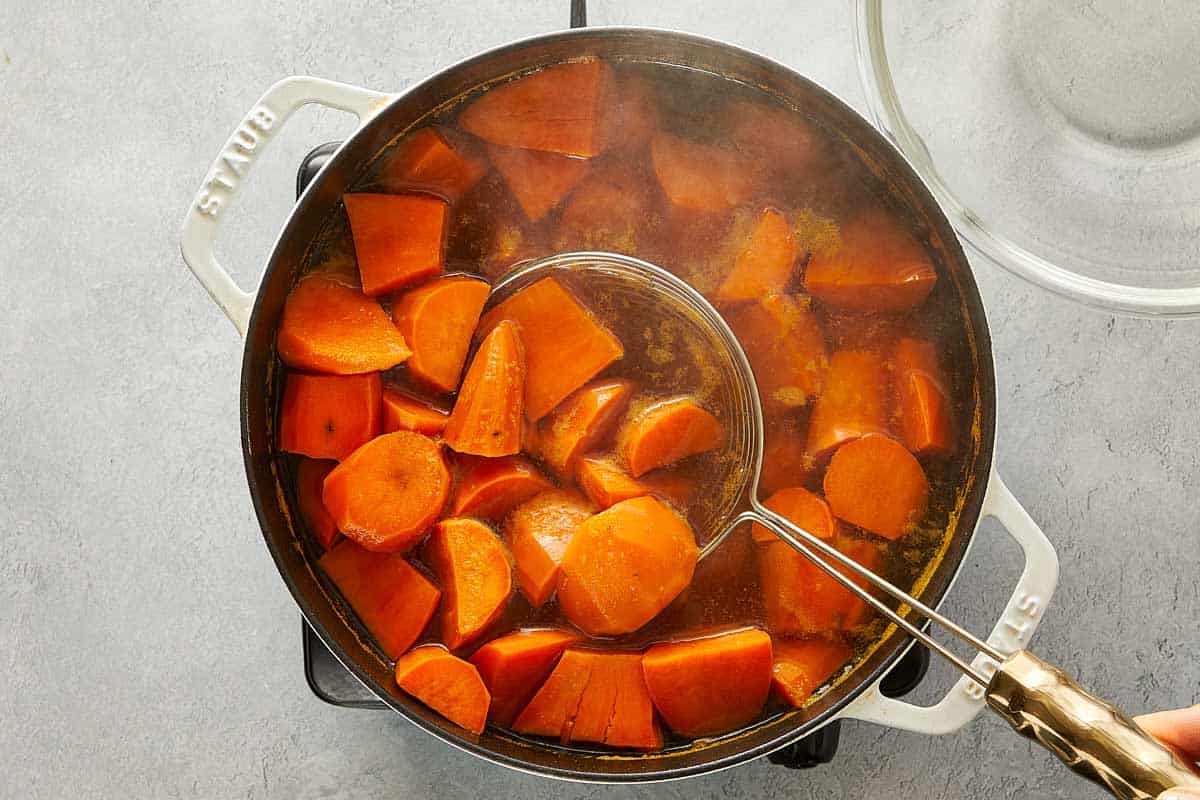Sweet potato chunks boiling in a large pot of water, with a skimmer lifting pieces out.