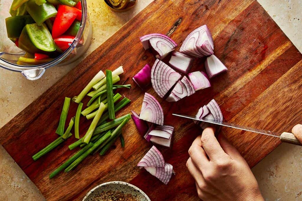 Chopping up the vegetables and cutting a red onion on a wooden chopping board