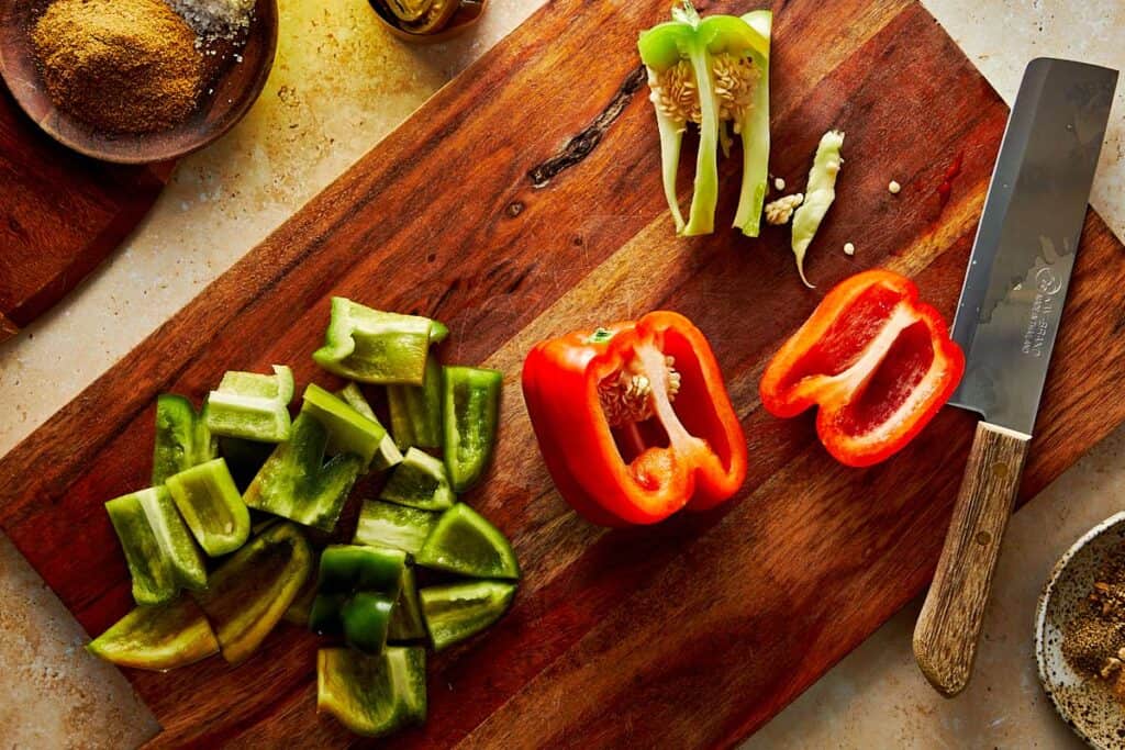 bell peppers green and red being chopped up on a wooden chopping board