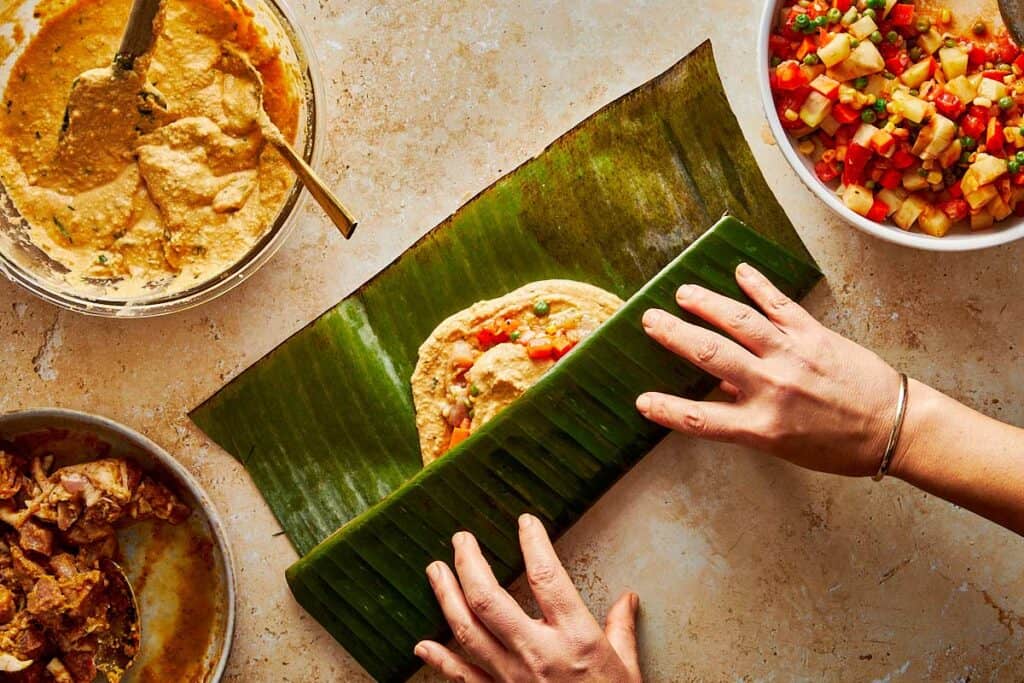 wrapping tamales paste in a green banana leaf with the leaf in half